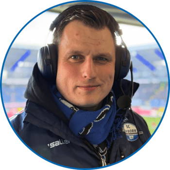 Porträt von Reporter Dirk Hoffmann in der Home Deluxe Arena. Er hat kurze braune Haare und trägt einen SCP07-Schal, den er in den Ausschnitt seiner dunkelblauen Winterjacke gesteckt hat.