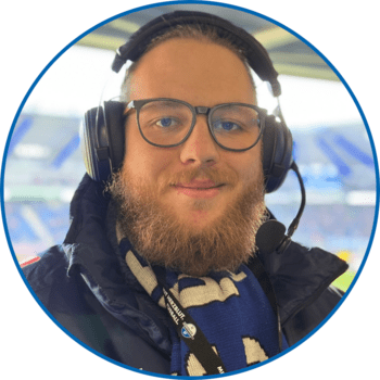Porträt von Reporter Oskar Auffenberg in der Home Deluxe Arena. Er trägt seine blonden Haare zum Zopf zusammengebunden, eine runde Brille, einen Vollbart sowie einen SCP07-Schal über seiner dunkelblauen Winterjacke.
