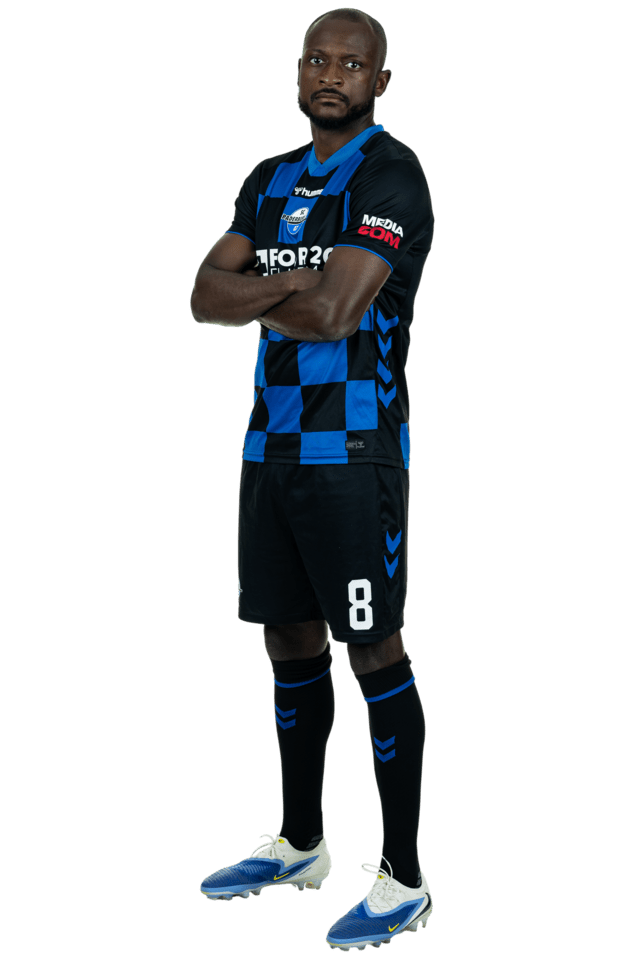 David Kinsombi steht leicht nach links eingedreht mit verschränkten Armen. Er trägt das aktuelle Heimtrikot.