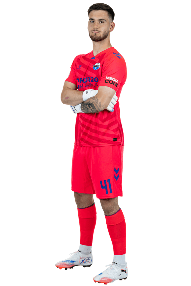 Dennis Seimen steht leicht nach links eingedreht mit verschränkten Armen. Er trägt das aktuelle pinke Torwarttrikot.