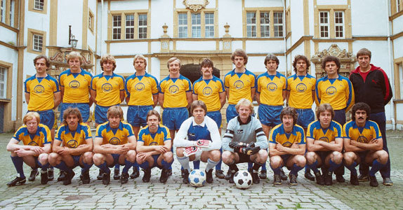 Mannschaftsfoto der Neuhäuser Aufstiegsmannschaft von 1982 im Innenhof des Residenzschlosses. Die Mannschaft trägt gelbe Trikots mit blauem Kragen sowie blaue Hosen.